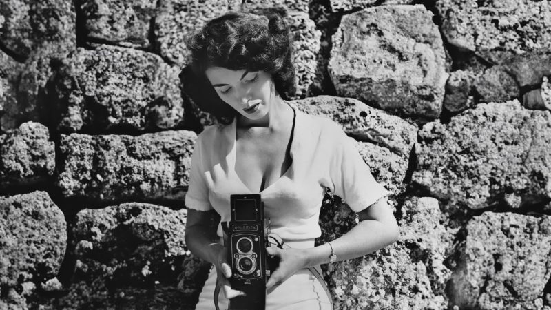 black-and-white photo of photographer Bunny Yeager taking a self-portrait with a midcentury camera
