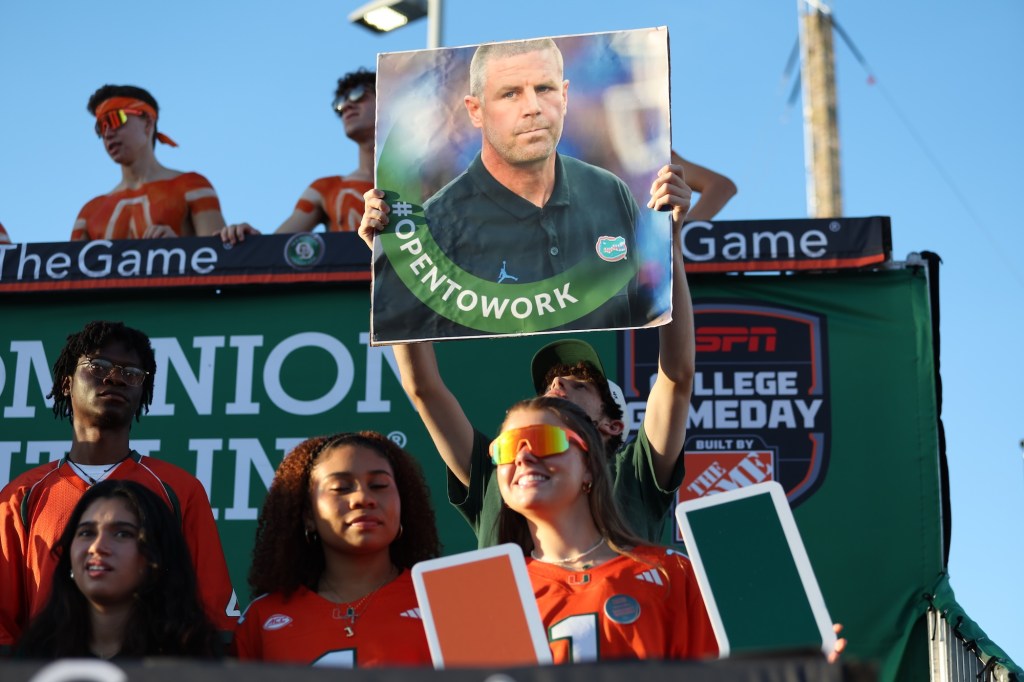 UM fans hold up a poster with a photo of Gators coach Billy Napier. The poster reads, "Open to Work"