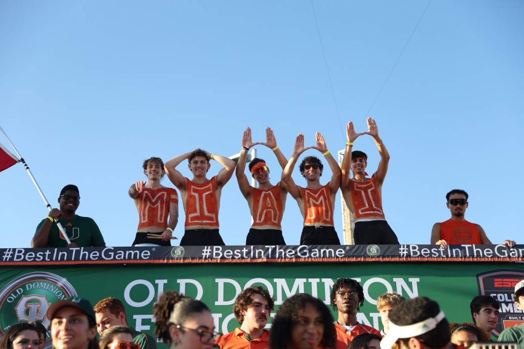 a group of sports fans stands on a platform wearing paint on their chests with text reading "Canes"