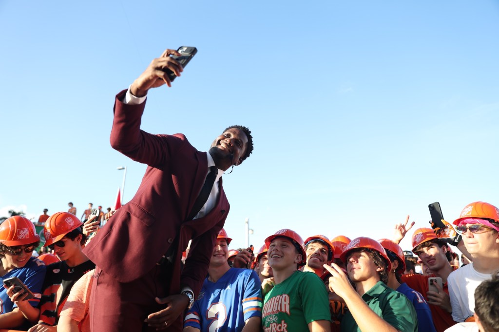 a man in a maroon suit takes a selfie with UM fans at a tailgate