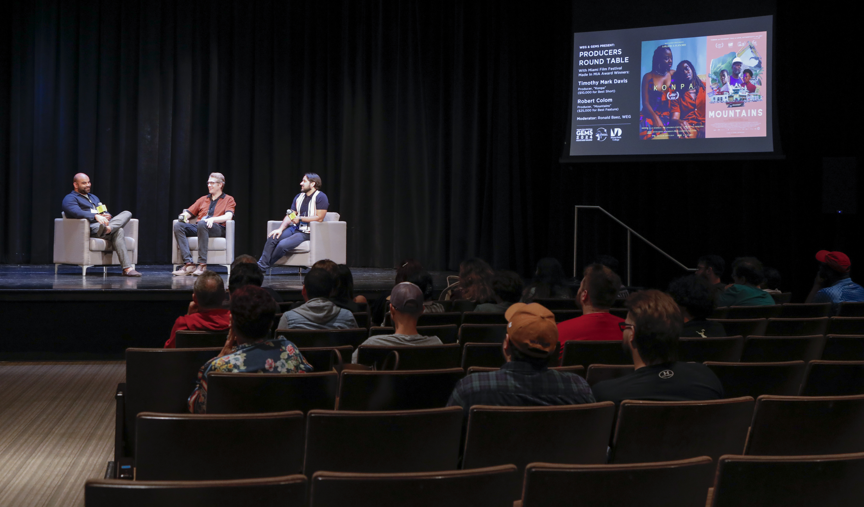 a panel of filmmakers speaks on a stage in front of an audience in a theater