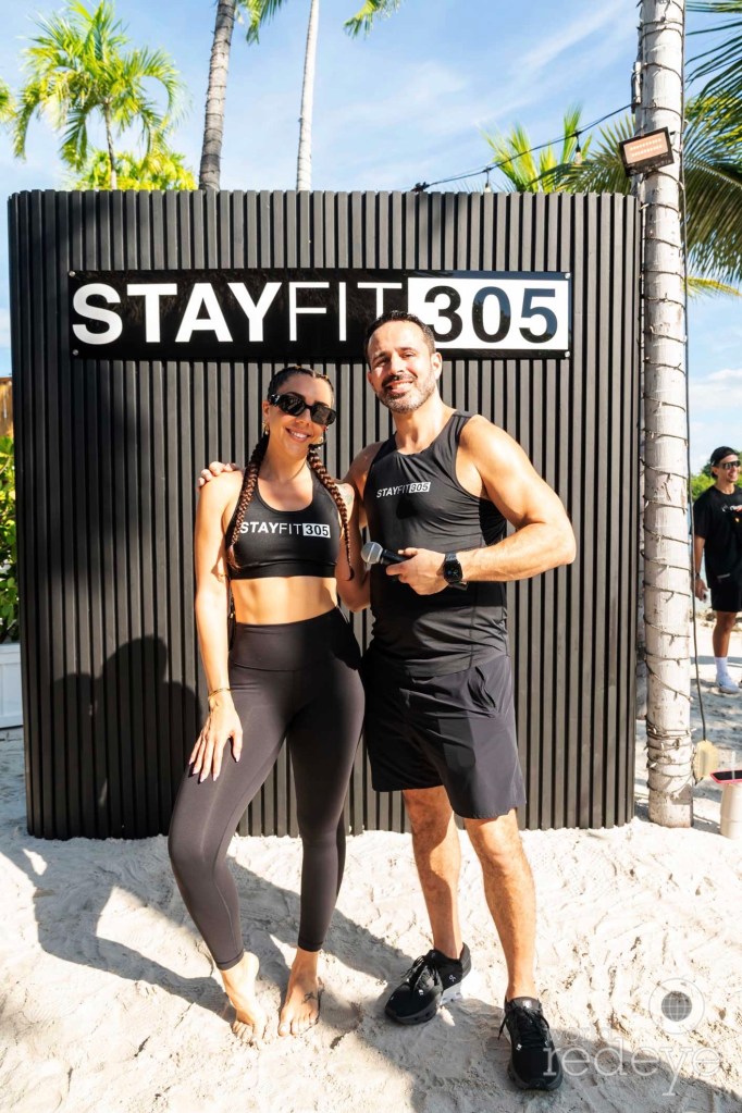 Two people in athleisure reading, "Stay Fit 305" pose in front of a photo opp wall reading, "Stay Fit 305"