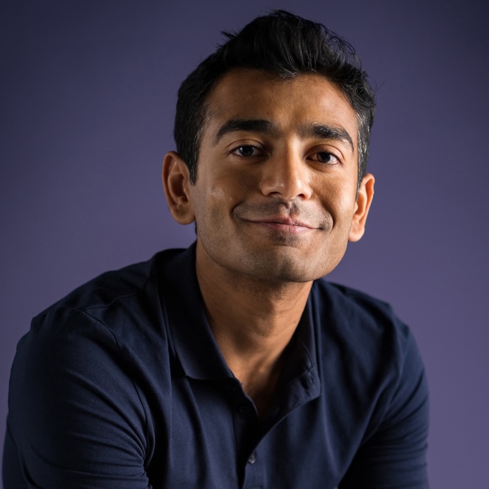 color photo of a smiling dark-haired man wearing a navy-blue shirt
