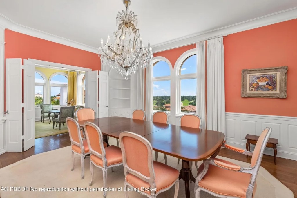 Depicted is a coral-colored dining room with an ornate chandelier hanging from a stark white ceiling.