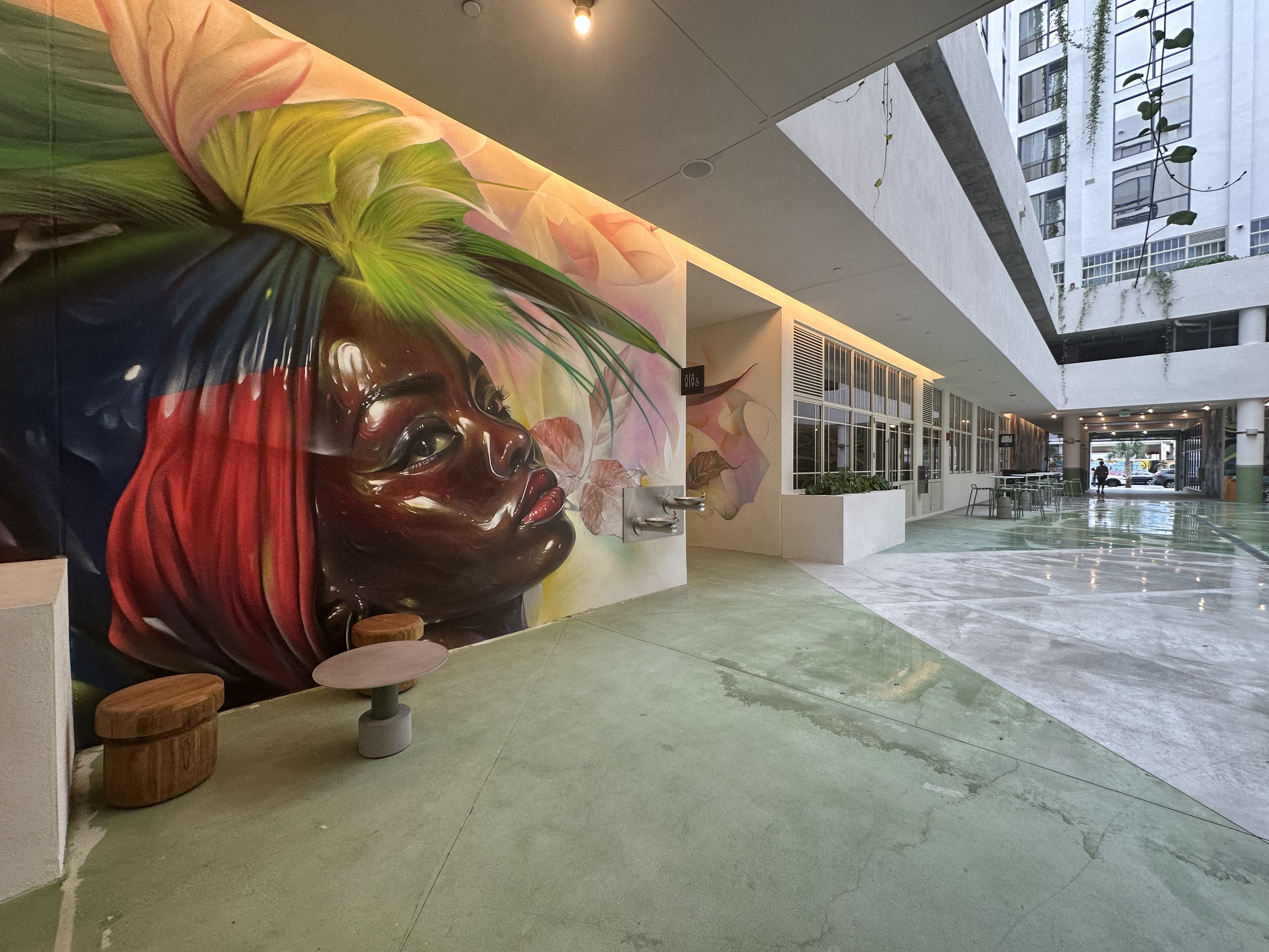a mural of a Black woman in a red and blue headdress on the wall of an outdoor courtyard