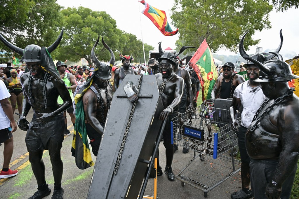 a group of men covered in black paint, wearing helmets with horns, march a black coffin in a procession