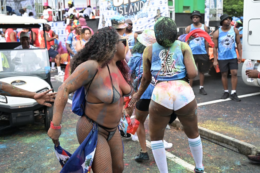 two women splattered in paint dance in front of a gold cart at a festival
