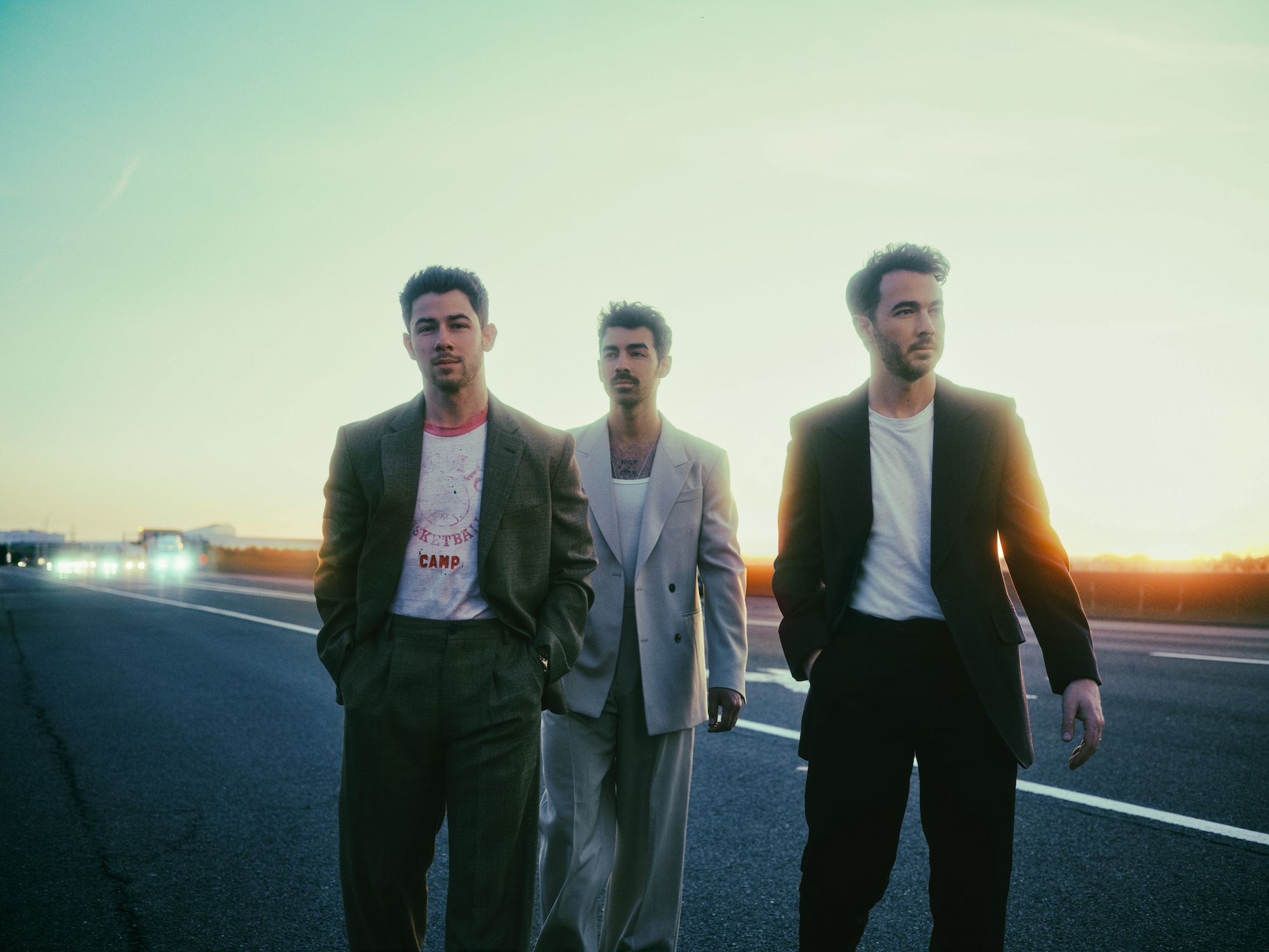 backlit portrait of the Jonas Brothers on a road wearing T-shirts with slacks and blazers