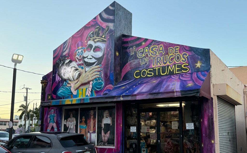 a costume store with a muraled entrance depicting comedy and tragedy masks, a clown, and writing reading, "La Casa de los Trucos Costumes"