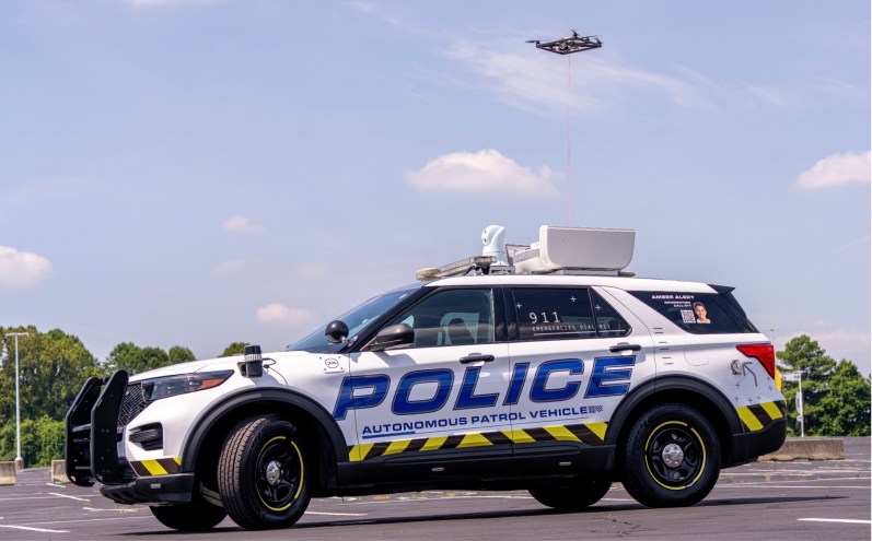 Depicted is an autonomous police patrol SUV with a drone flying overhead