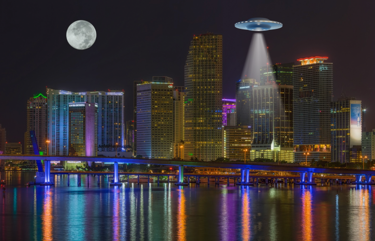 Depicted is a cartoon flying saucer overlaid onto a photo of the Miami skyline at night.