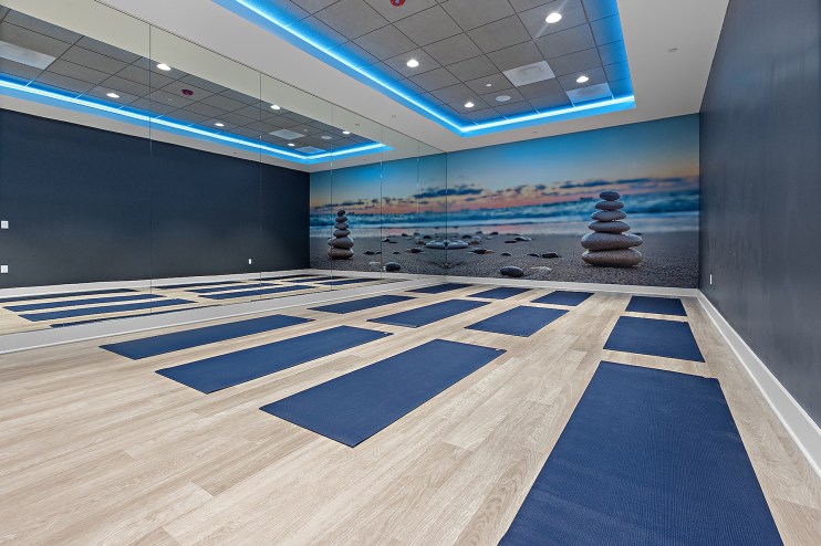 a room with yoga mats on the floor, a mirror wall, and a wall-sized close-up photo of rocks stacked on a beach