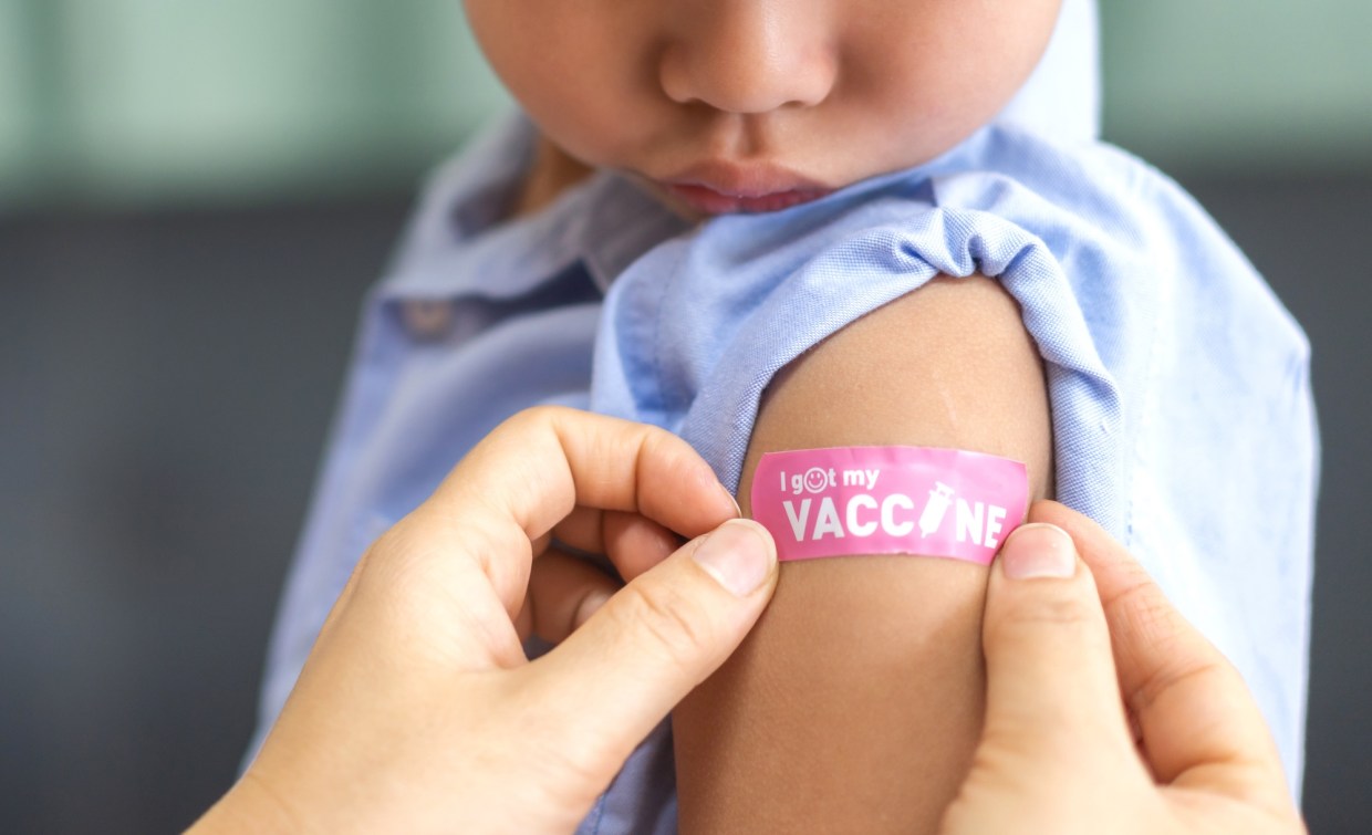Close-up photo of a small child getting a Band-Aid on their arm that says "I got my vaccine"