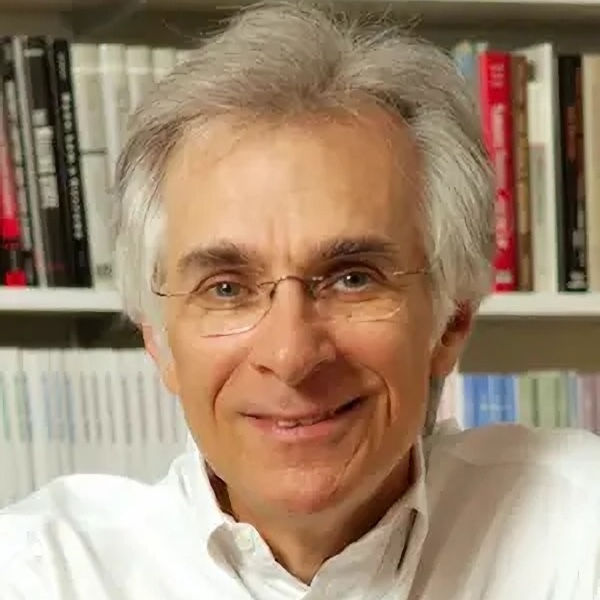 headshot of a gray-haired man wearing a white Oxford shirt and rimless glasses and posed in front of a bookshelf