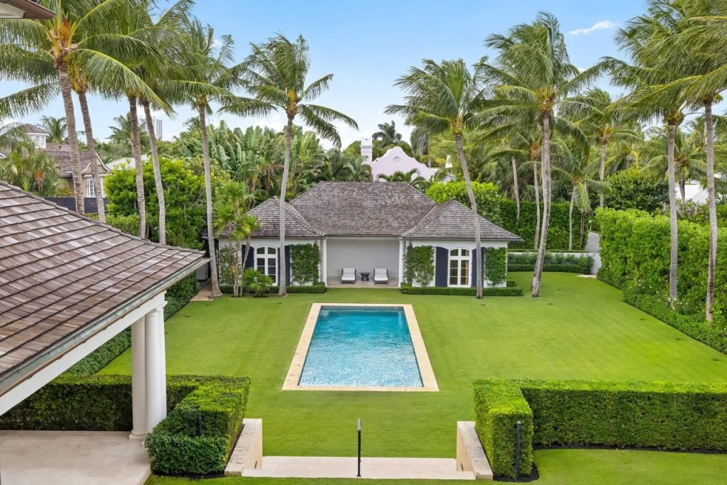 a rectangular pool sits in the middle of a lush backyard lawn and pool house