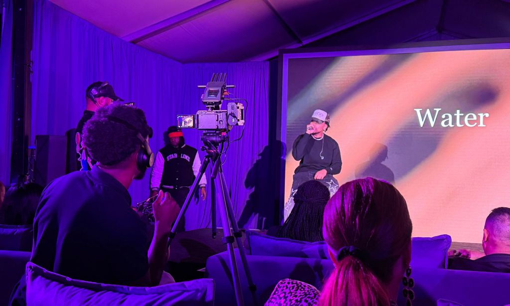 Photo of a young man performing on stage wearing a white baseball cap. 