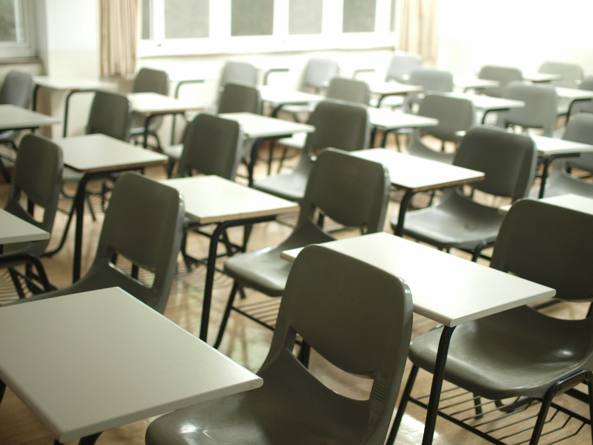 An empty classroom with rows of while desks and pale green chairs.