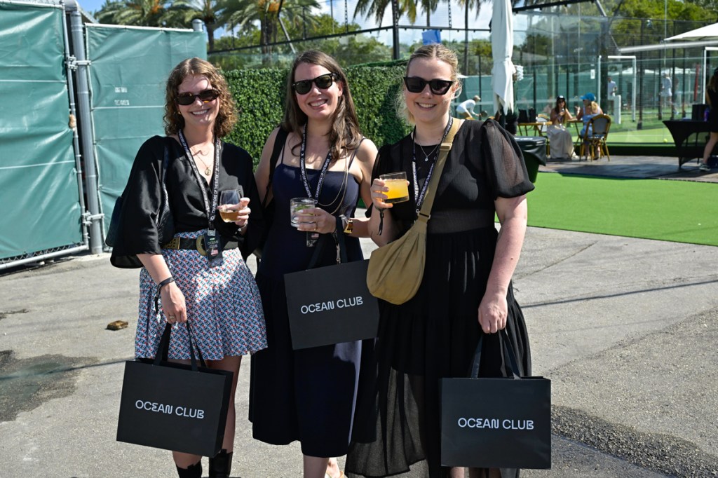 photo of three women posing in black outfits holding black shopping bags reading "Ocean Club"