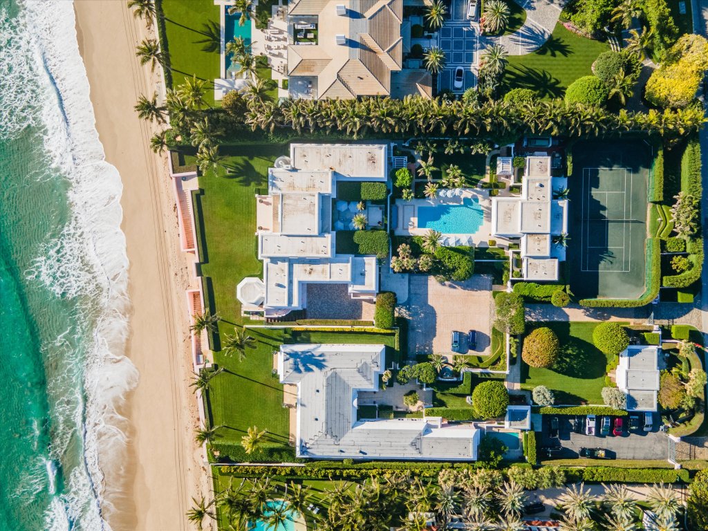 An aerial view of the estate shows four buildings, a tennis court, a pool, and ample parking