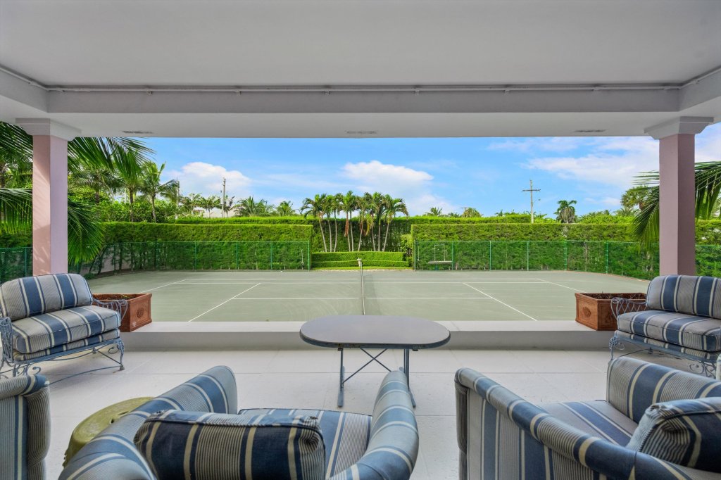 patio armchairs are arranged in a seating area adjacent to a full-sized tennis court replete with a shrub wall