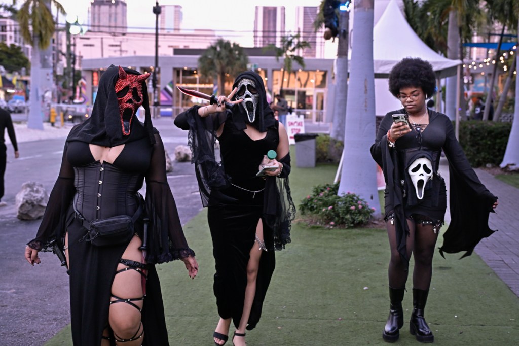 Photo of three people walking down the street in Scream masks on Halloween. One of the masks is rhinestoned red