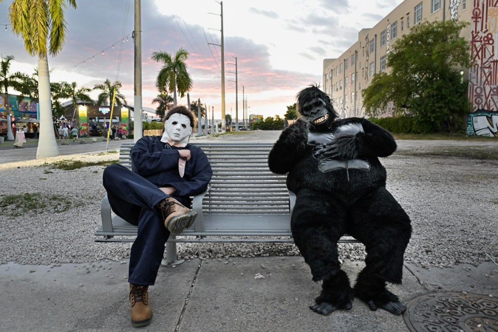 photo of a person dressed as Michael Myers and another dressed as a gorilla sitting on a park bench