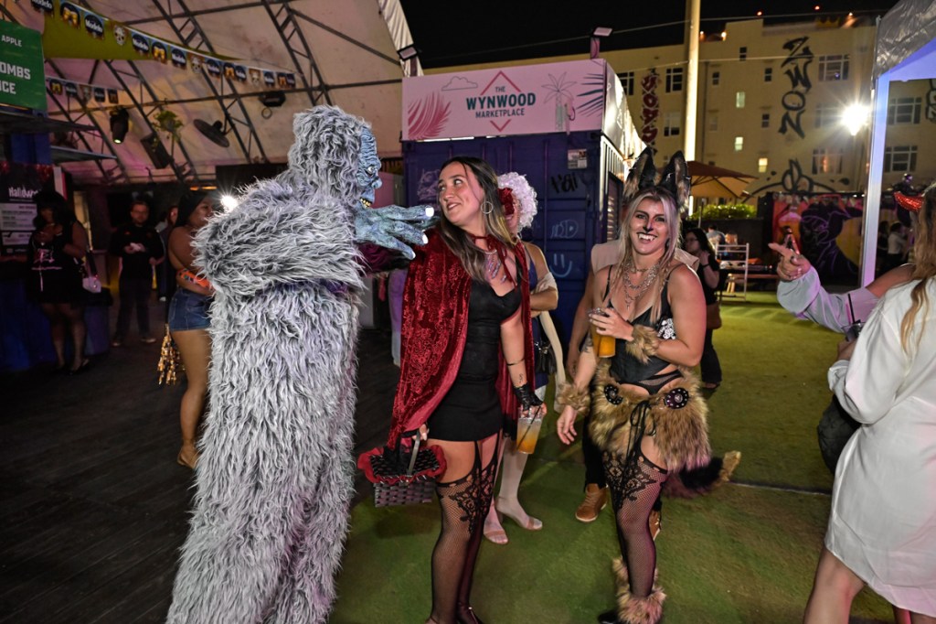 Photo of people dressed up for Halloween. A person in a hairy monster costume talks to a woman in a red cape