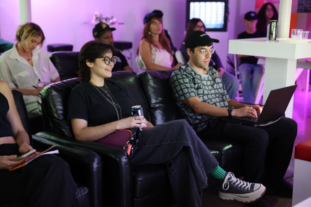 photo of a group of people sitting on black lounge chairs in a purple-lit room
