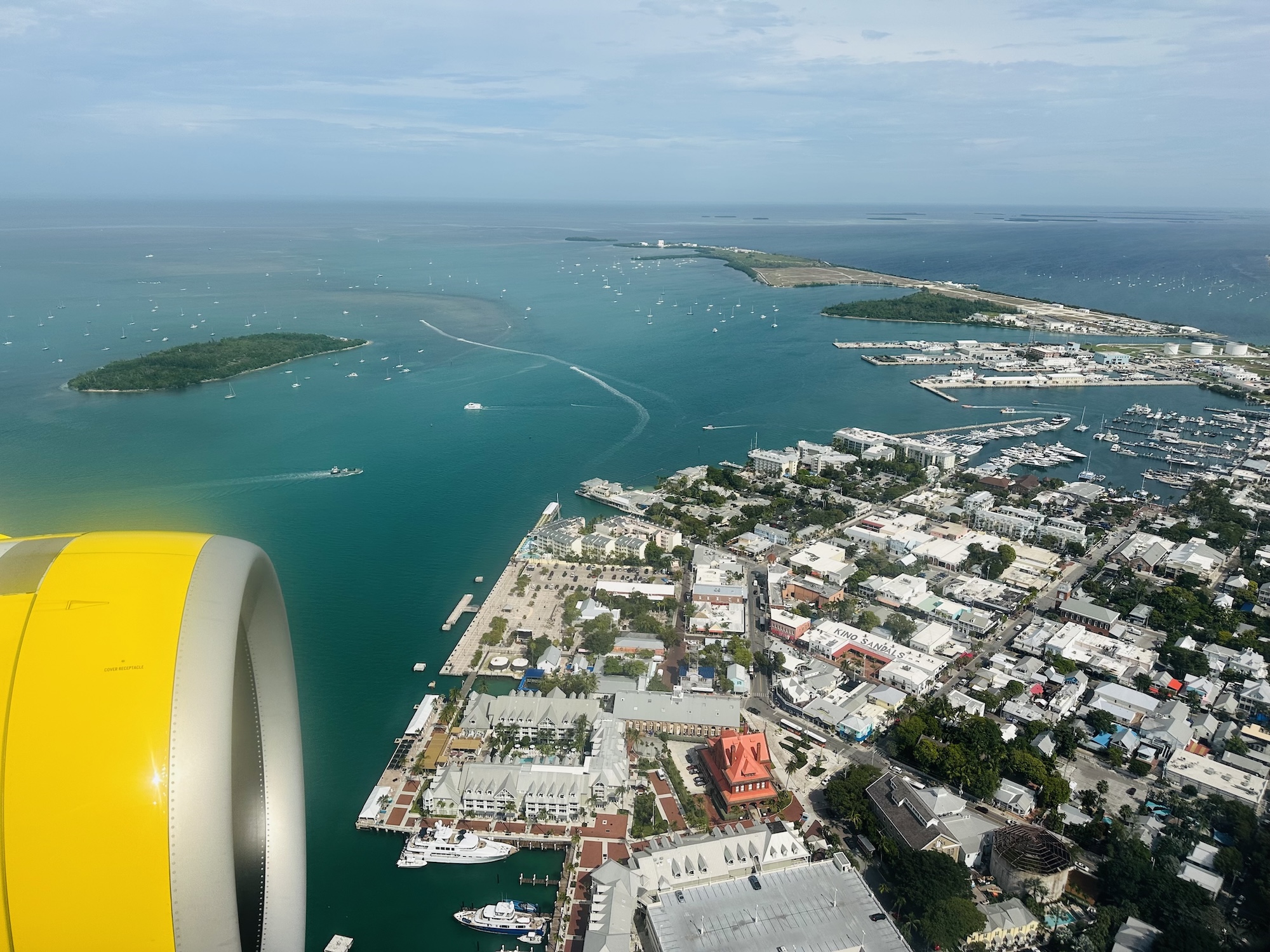photo of the view from an airplane flying over homes and businesses in Key West, Florida, with part of the plane's yellow engine visible from the window