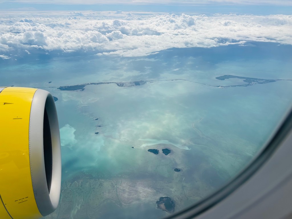 photo of the view from an airplane flying over the ocean with part of the plane's yellow engine visible from the window