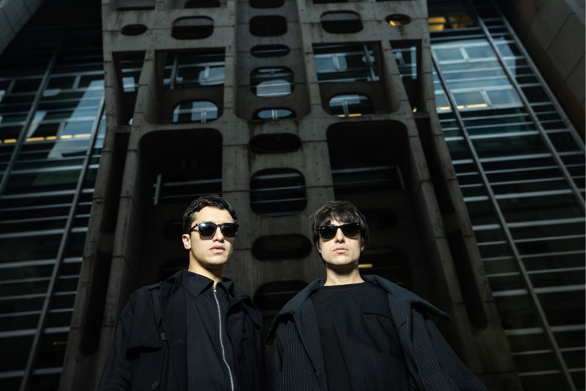 picture of two man wearing black in front of a black building.