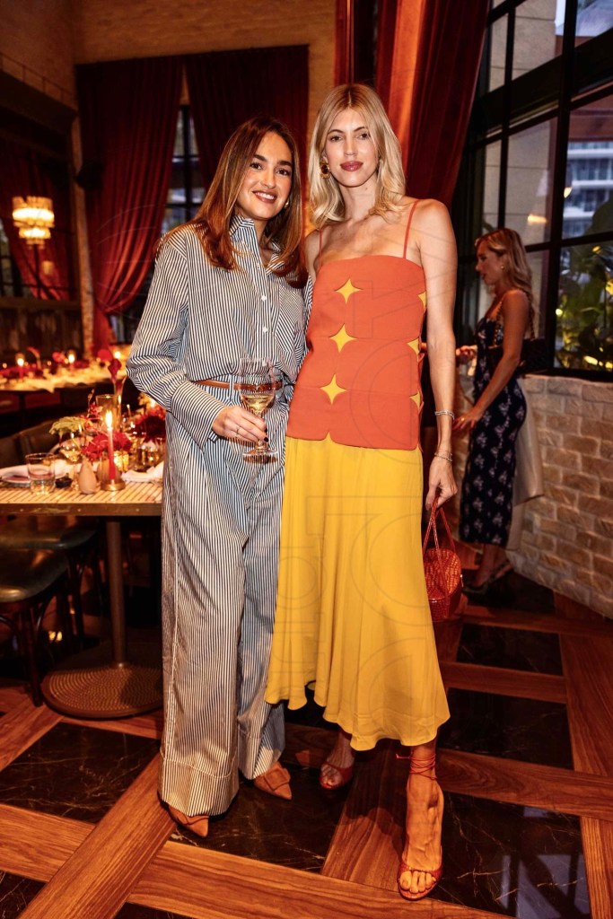 photo of two women in cocktail wear posing in front of two long, candle-lit dinner tables 