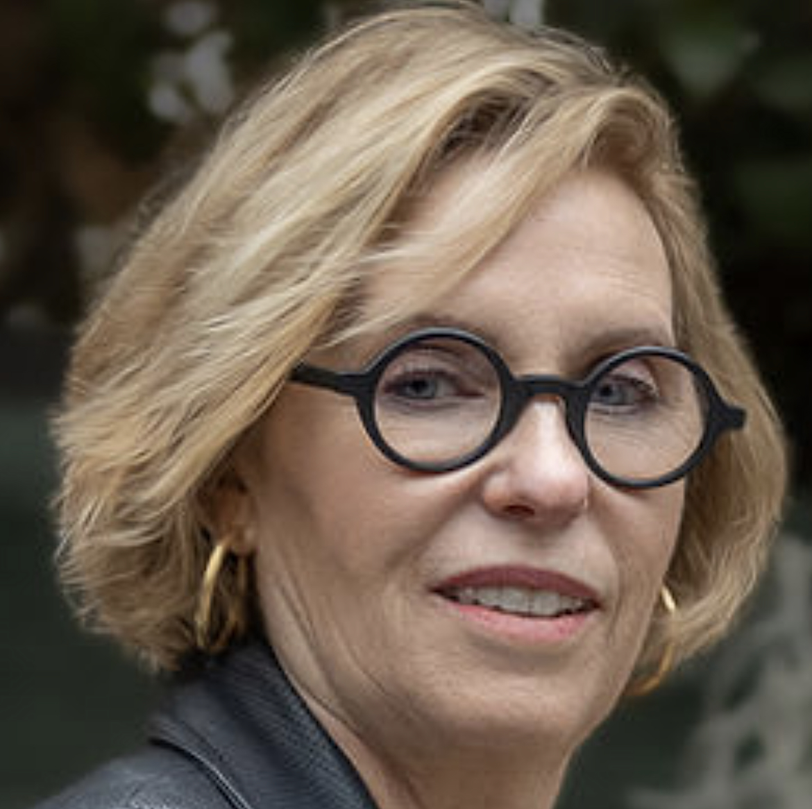 three-quarters headshot of a woman with a blond bob haircut and round-rimmed glasses