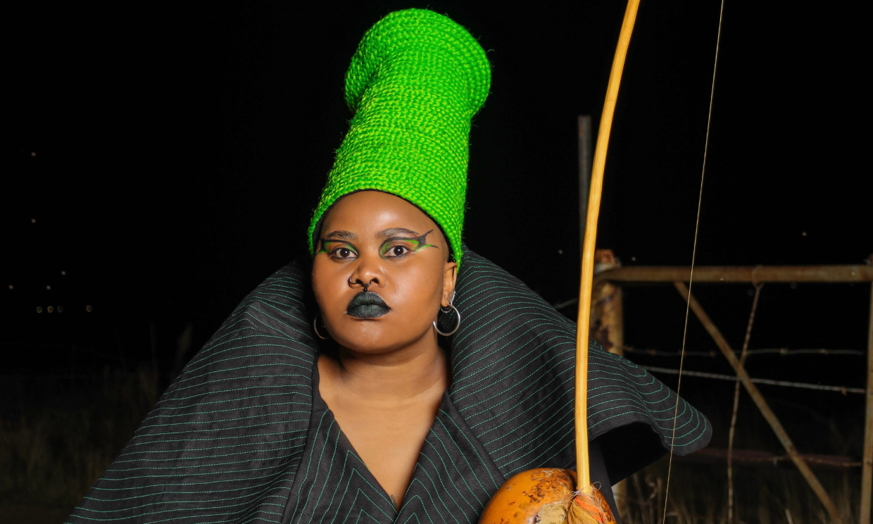 Photo of an African woman wearing a green hat and holding an instrument in her left hand.