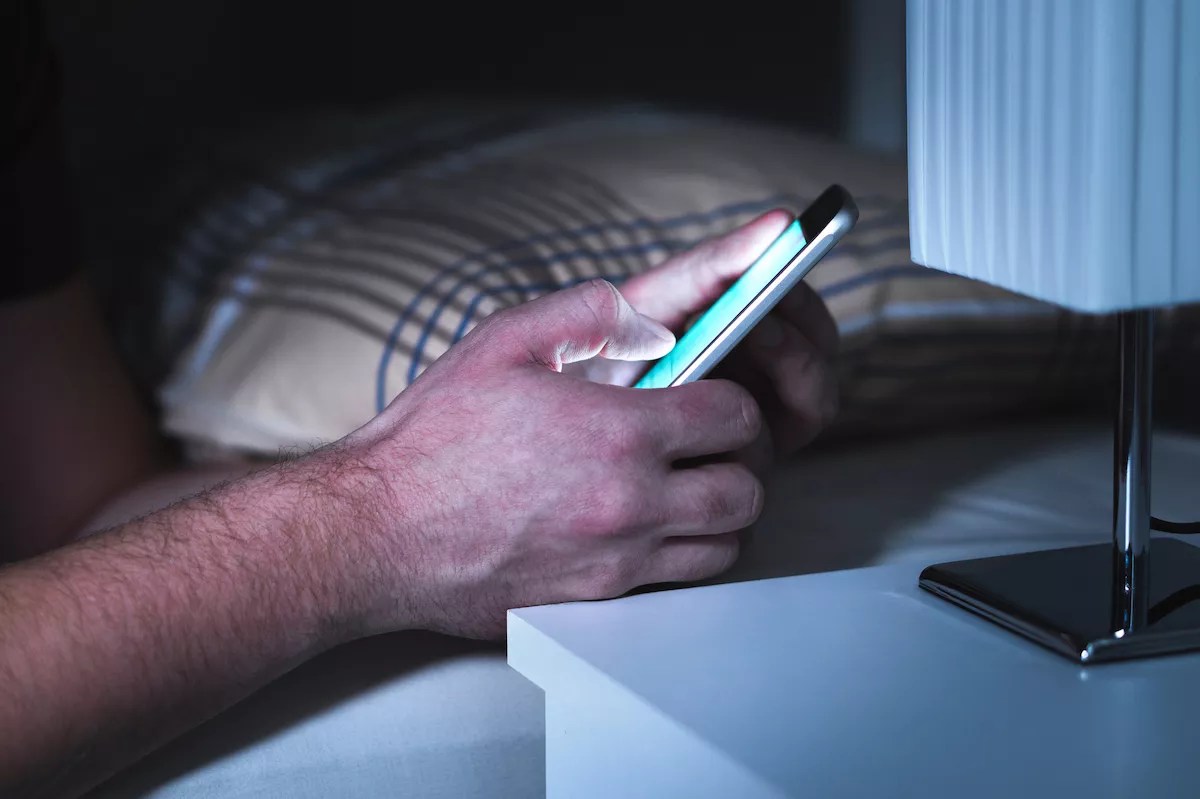 closeup of a man's hand texting in bed