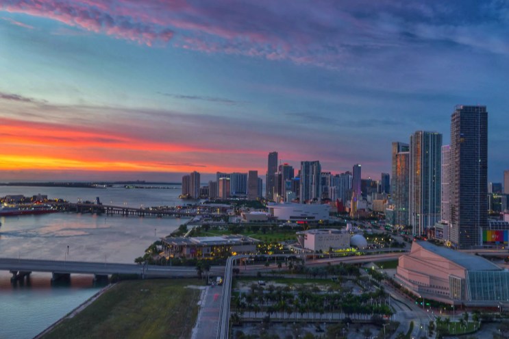 The sun sets on the Miami skyline, casting shades of pink and orange into the sky.