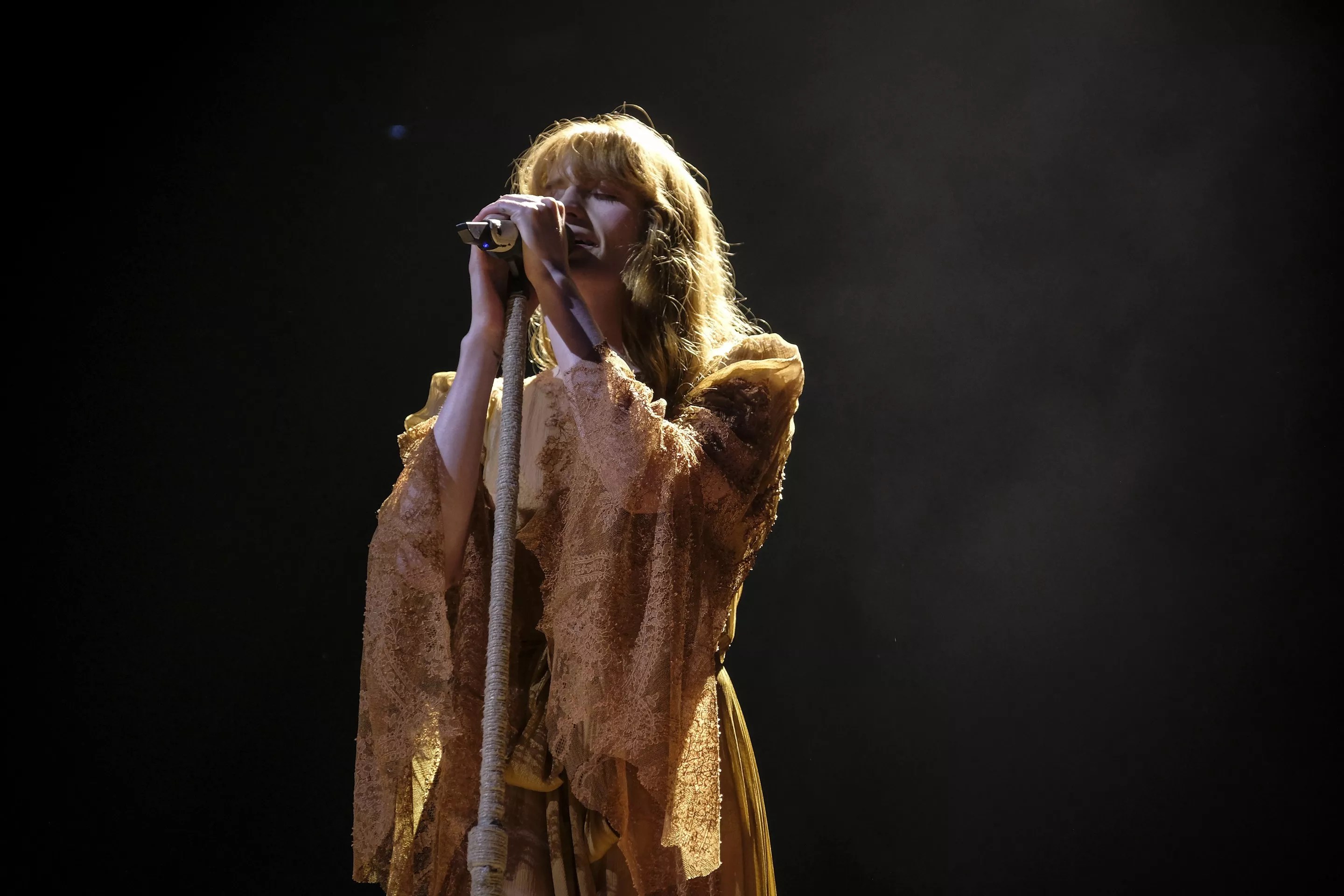 Picture of a woman wearing a yellow dress singing on stage holding a microphone.