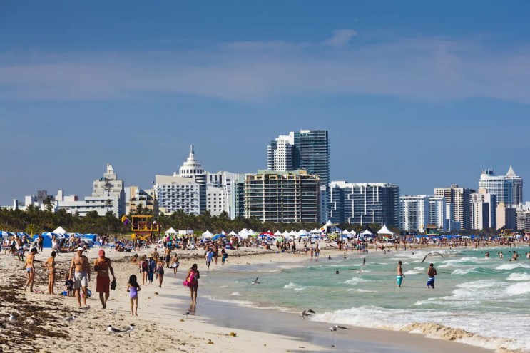 A Miami beach with people walking along it in front of the skyline