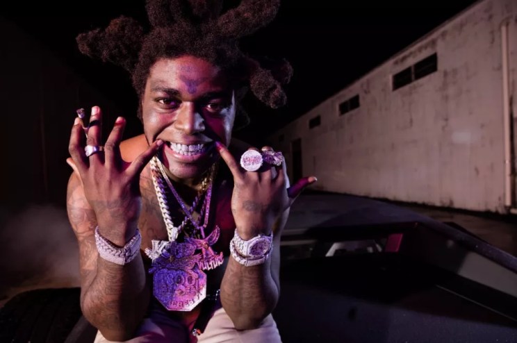 Closeup color photo of Kodak Black at night, showing off bling and grill