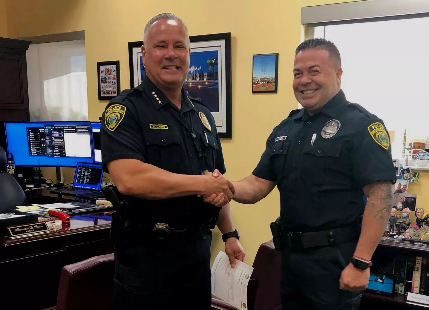 two uniformed police officers shake hands and smile at the camera