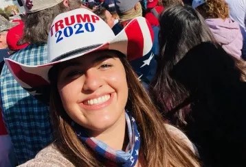 color photo of a smiling young woman wearing a white, red, and blue Trump 2020 hat