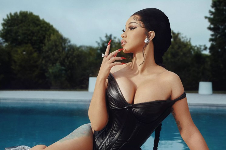 Rapper Cardi B sitting poolside in a black leather swimsuit