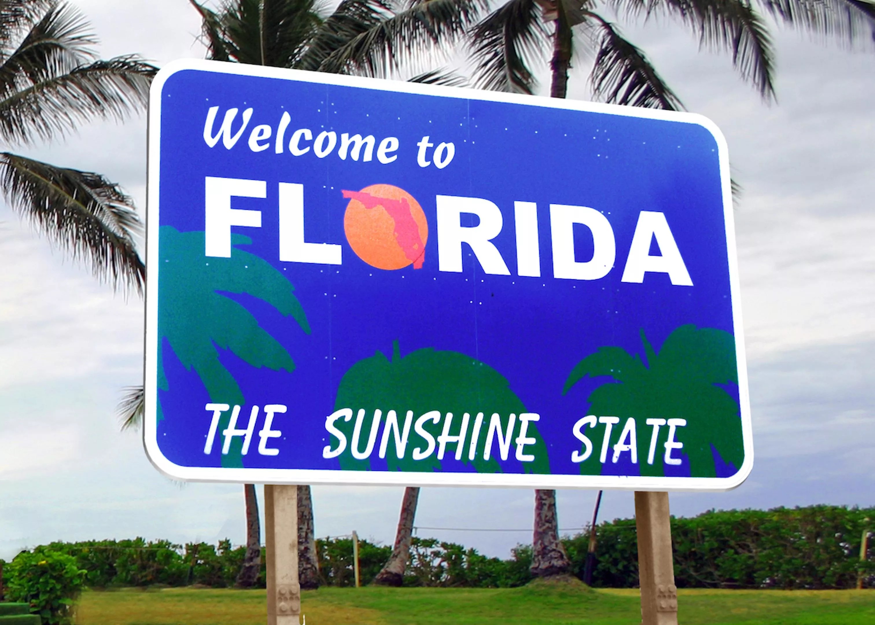 A royal blue "Welcome to Florida, The Sunshine State" sign surrounded by palm trees.