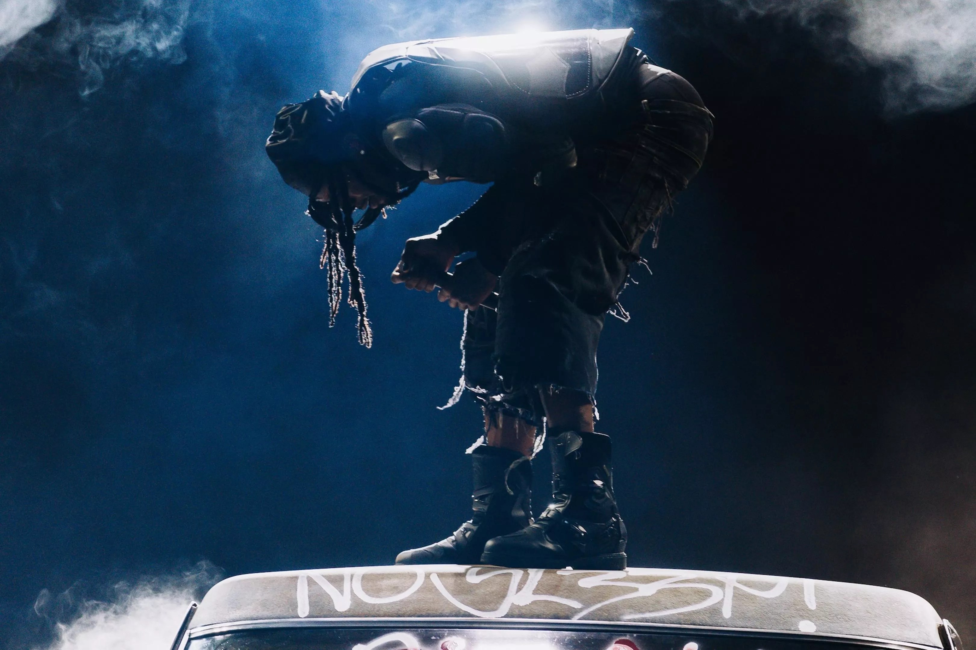 Playboi Carti performing on stage atop the hood of a car