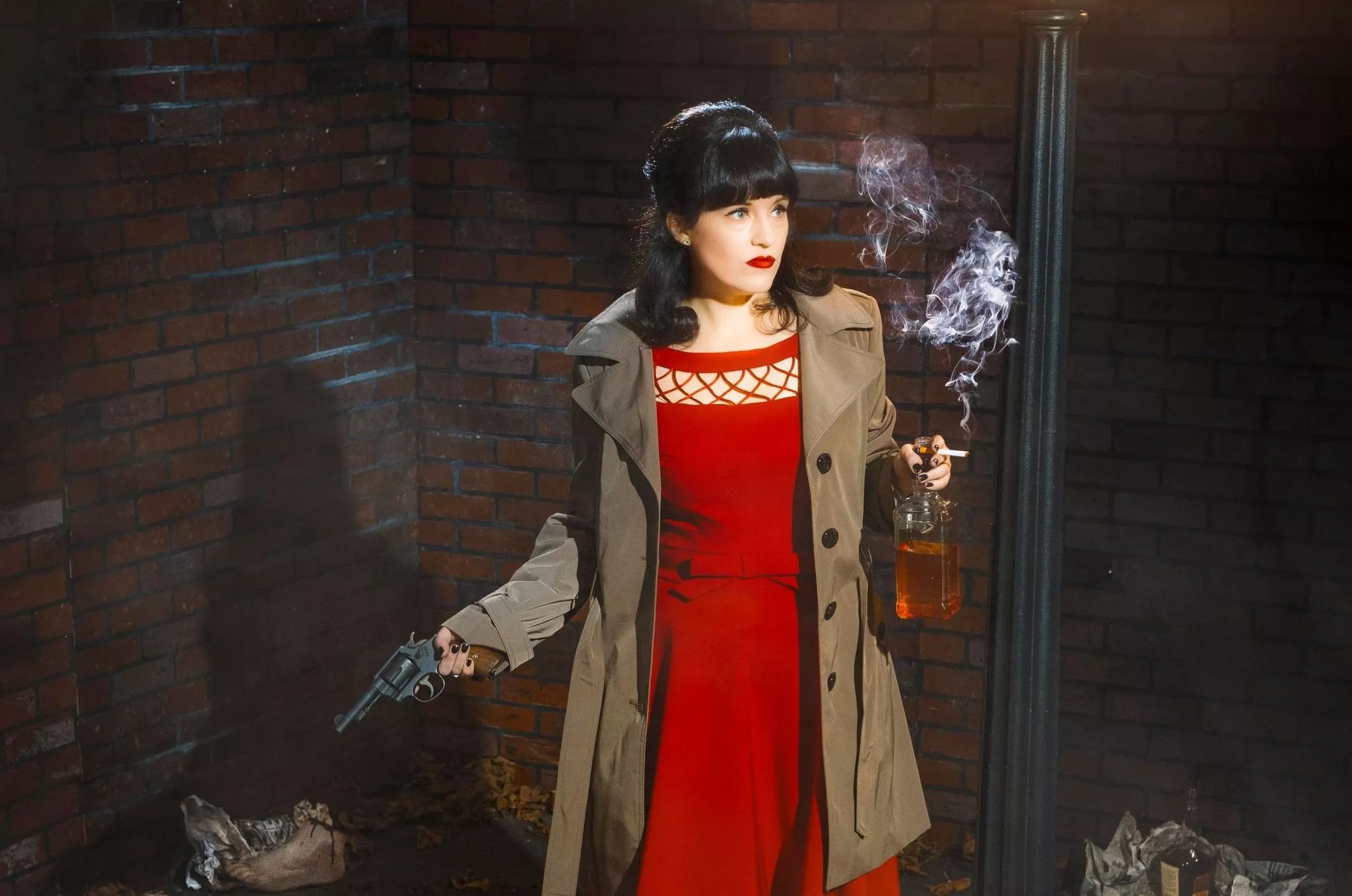 Improv performer in a red dress holding a gun, bottle of whiskey, and cigarette