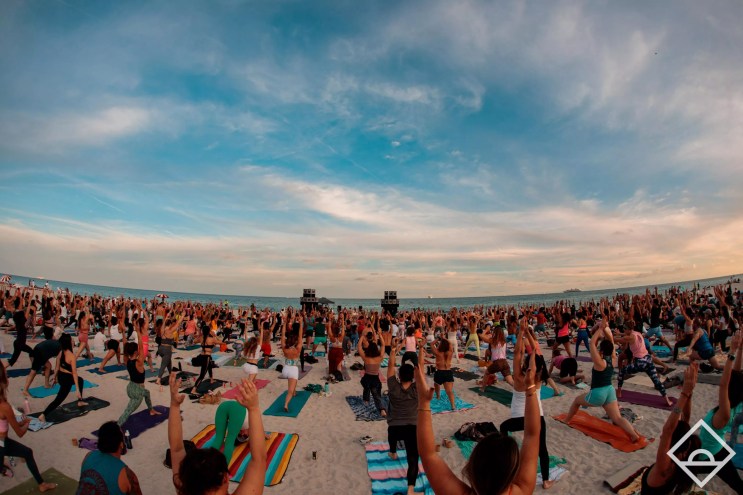 A large group of people doing yoga on the beach at dawn