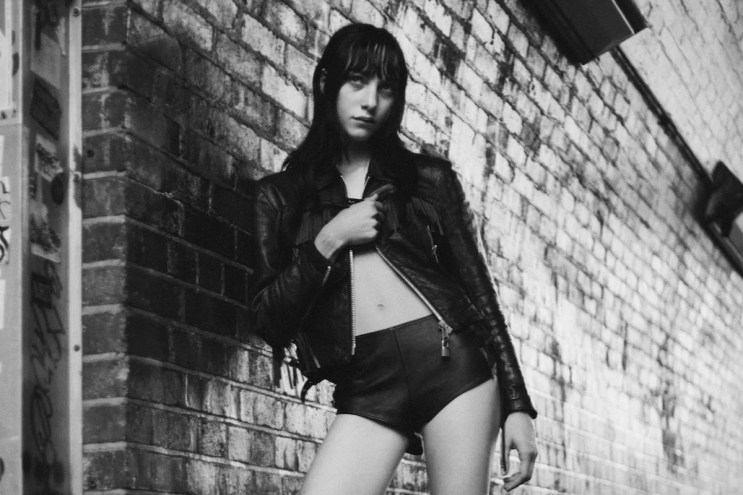 Black and white photo of Devon Ross leaning on a brick wall