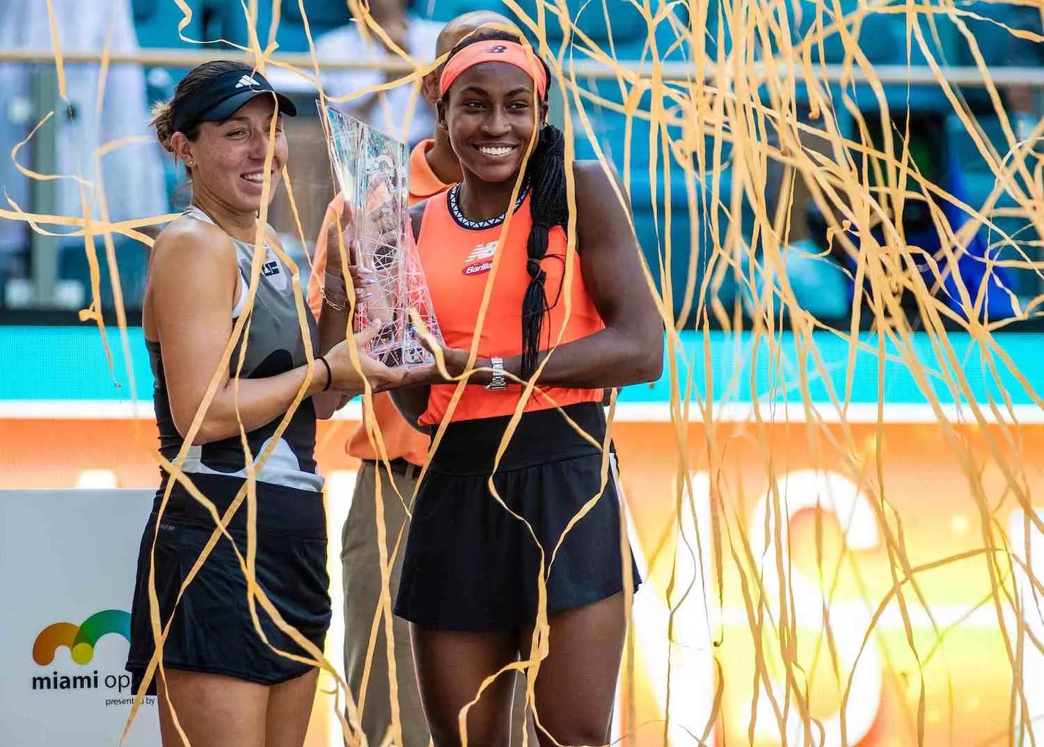 Color photo of two smiling women's tennis professionals holding a glass trophy