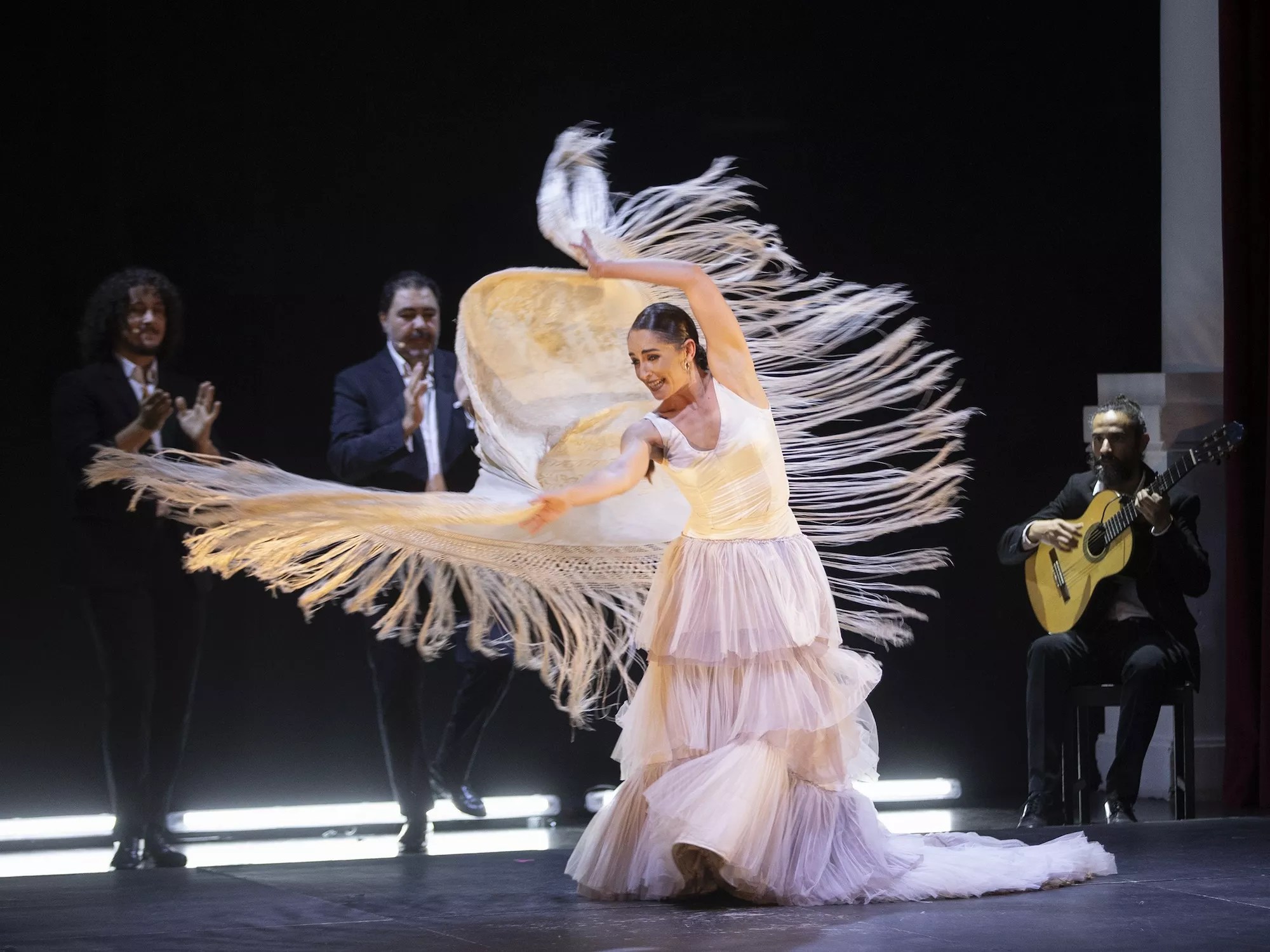 Flamenco dancer on stage in a white costume as the fringe moves in the air