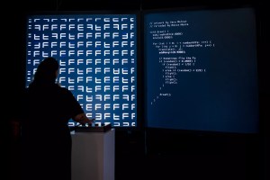 A person stands in front of a large projection of code